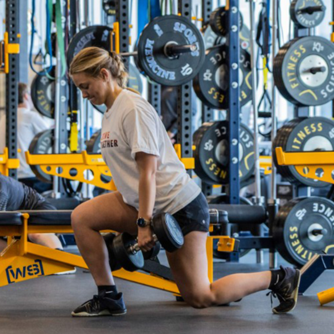 Woman does a lunge with two barbells at fitness science in rochester new york