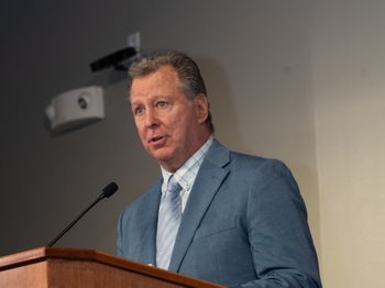 A man with short light-colored hair speaks at a podium.