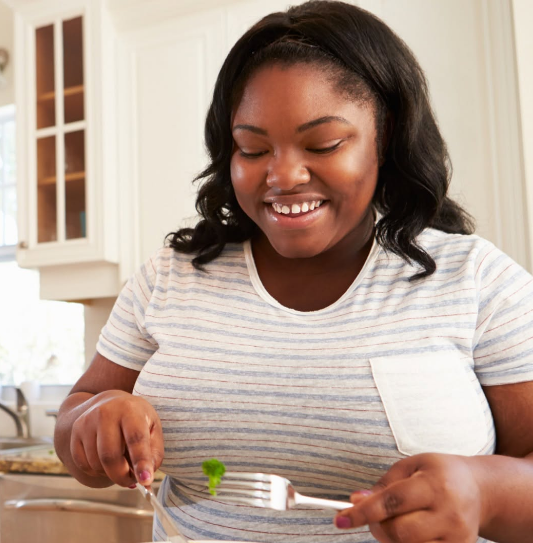 Woman smiling looking at fork with vegetable on it