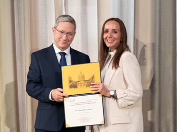 A woman with tanned skin and light brown hair accepts a certificate from a man with short grey hair.