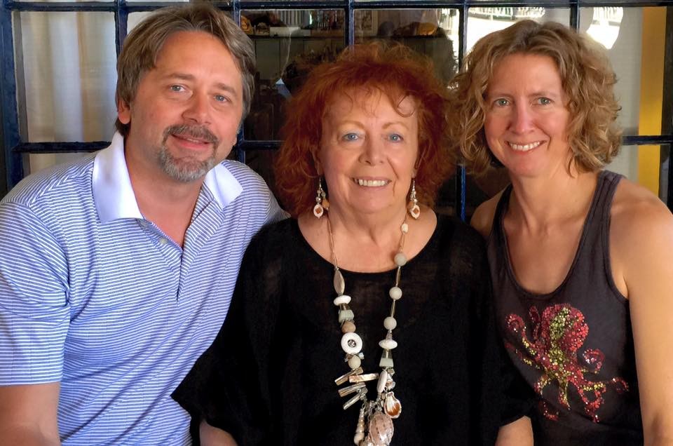 A man with short dark hair and a woman with curly blonde hair sit on either side of a woman with curly red hair.