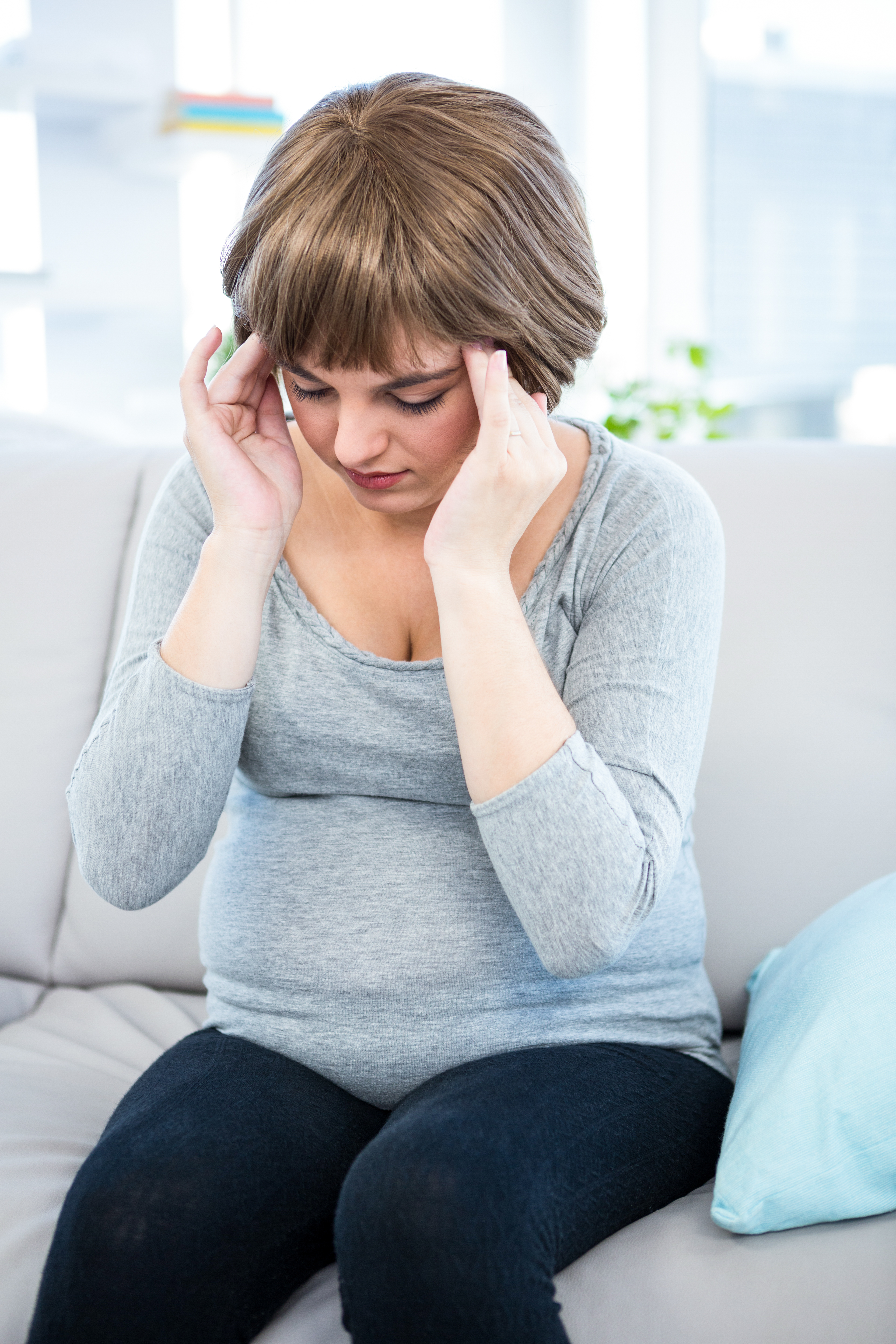 A pregnant person in a light blue shirt holds her head in pain