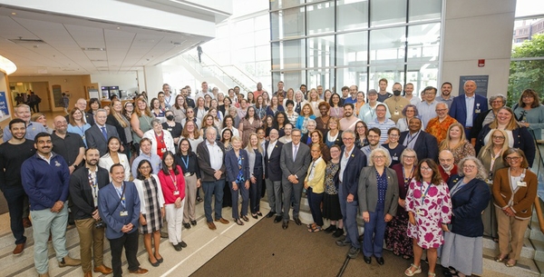 A large group of people standing on the stairs to the sunken room in the SRB atrium, smiling for the camera.