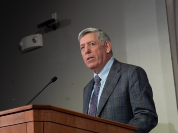 A man with short grey hair speaks at a podium.