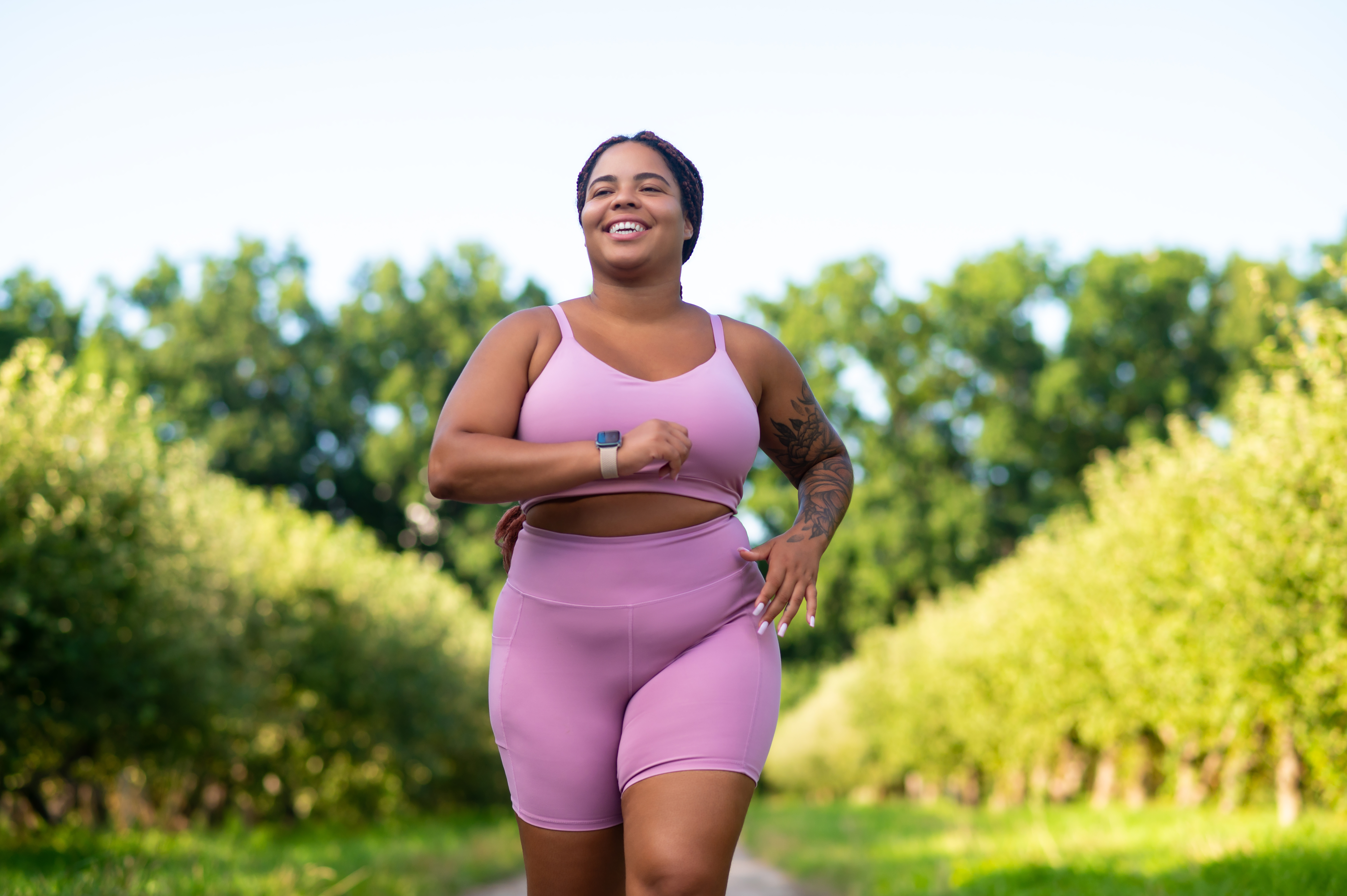 A woman in a pink outfit runs with greenery behind her
