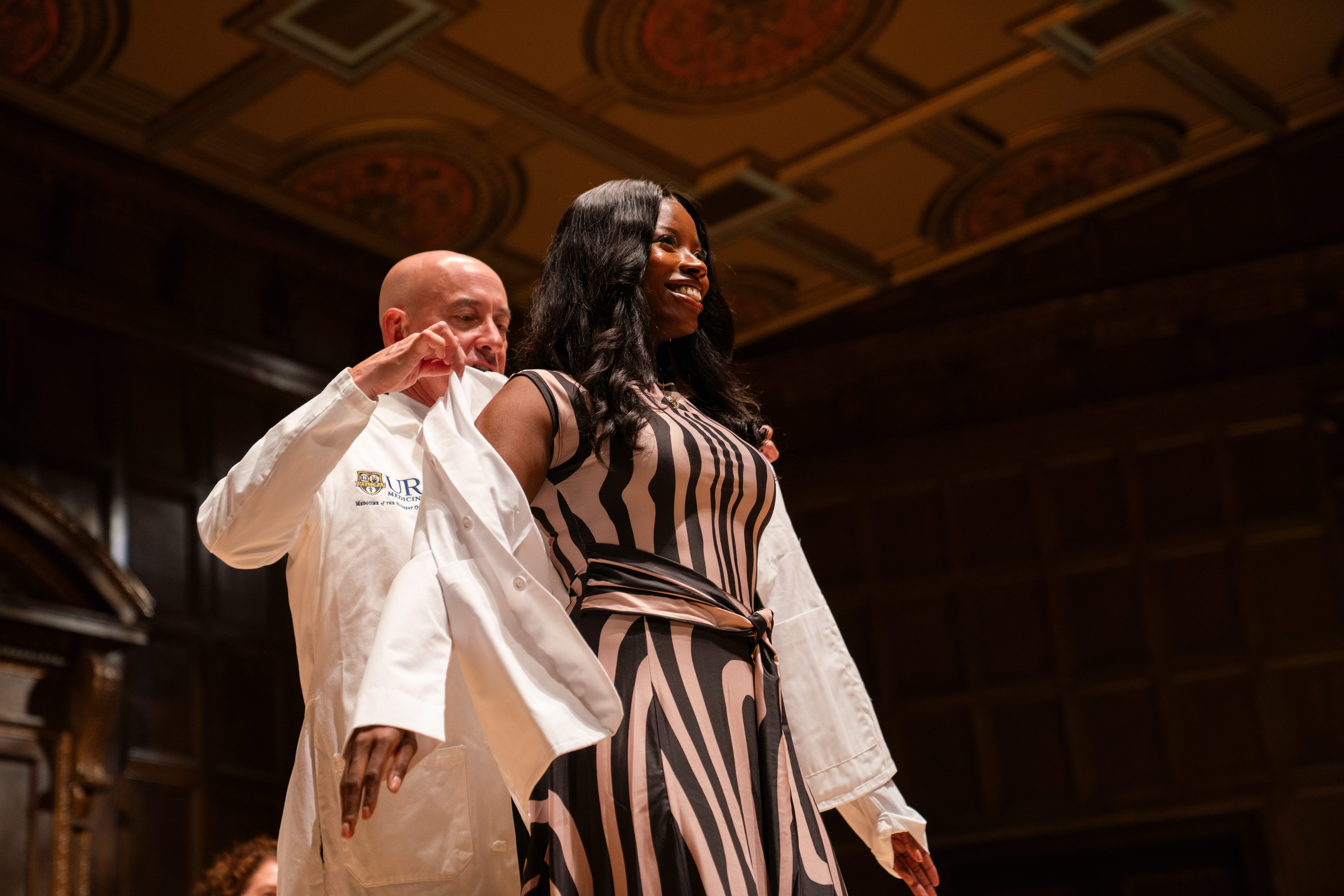 A student smiles while a white coat is placed around their shoulders at the 2026 White Coat Ceremony for URochester School of Medicine & Dentistry