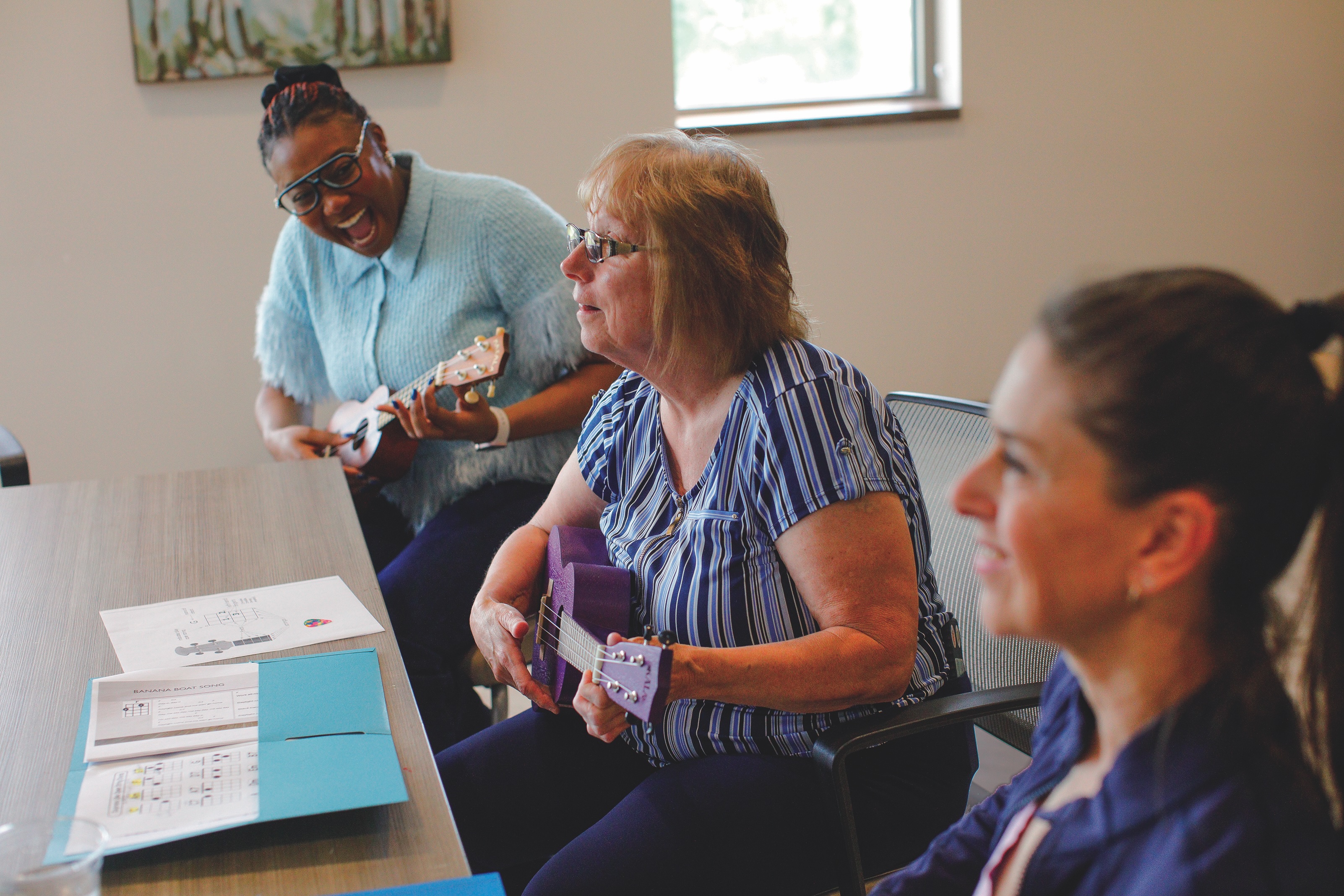 Medical student Kalese Goodwin sits with two patients, all playing the ukulele during a music therapy lesson.