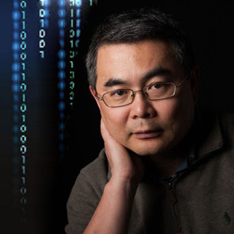 A man of Asian descent, with short greying hair. Behind him is a digital screen displaying vertical lines of binary code.