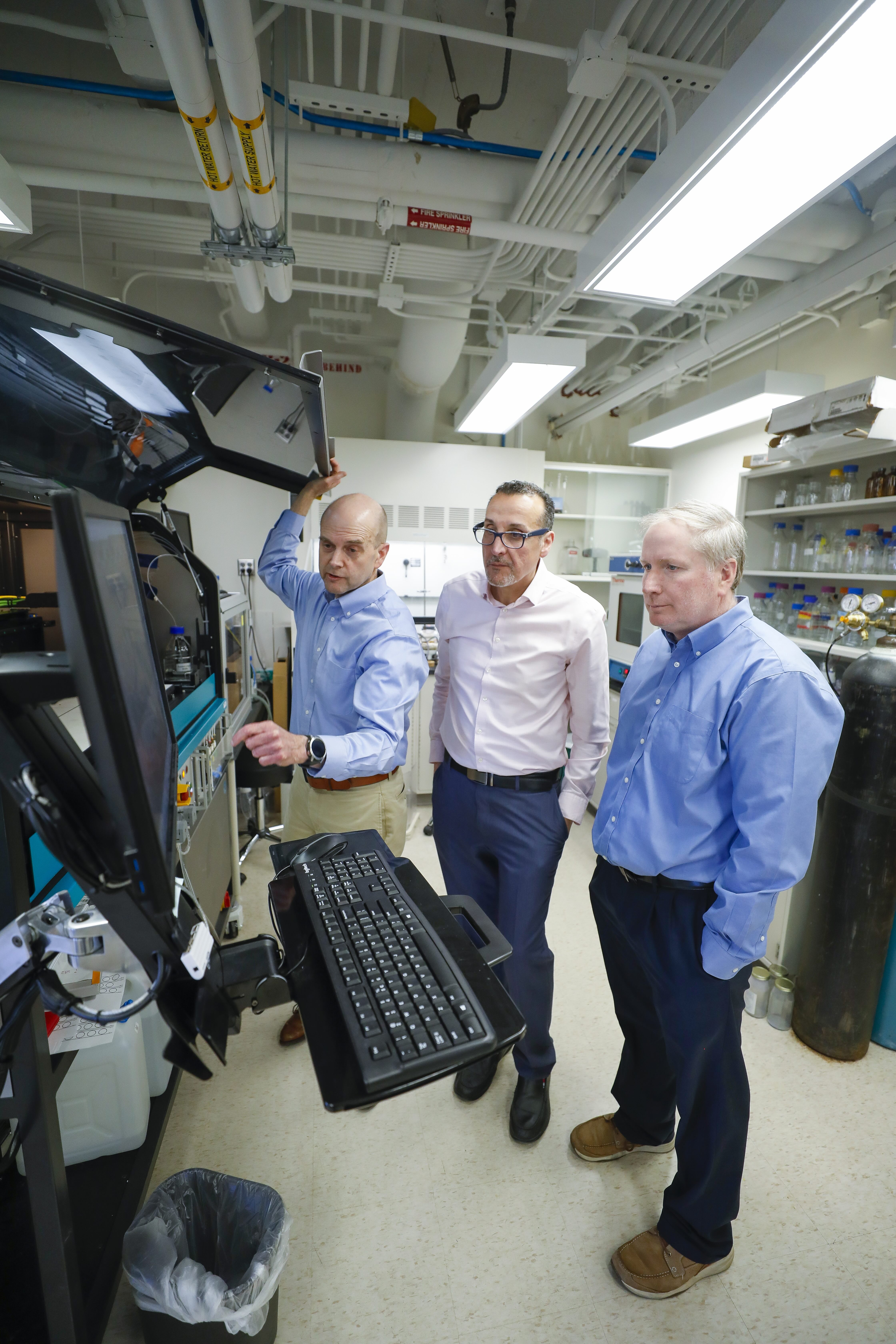 The three researchers looking at a specialized inkjet printer that shoots microscopic drops of antibody solutions onto the sensor chips.