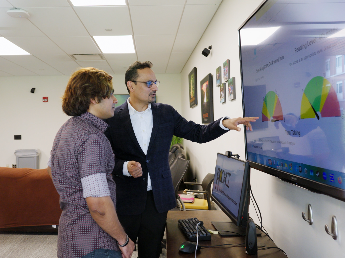 Two men look at a large screen displaying data graphics.