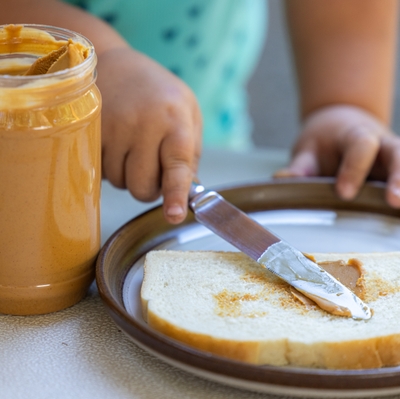 child spreading peanut butter on white bread