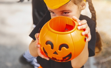 young girl holding halloween candy pumpkin up in front of face, smiling