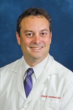 Man with wavy dark hair wearing a white shirt and tie.