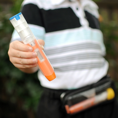 child in a striped polo showing the camera an auto-injector, with a carrying pouch on.