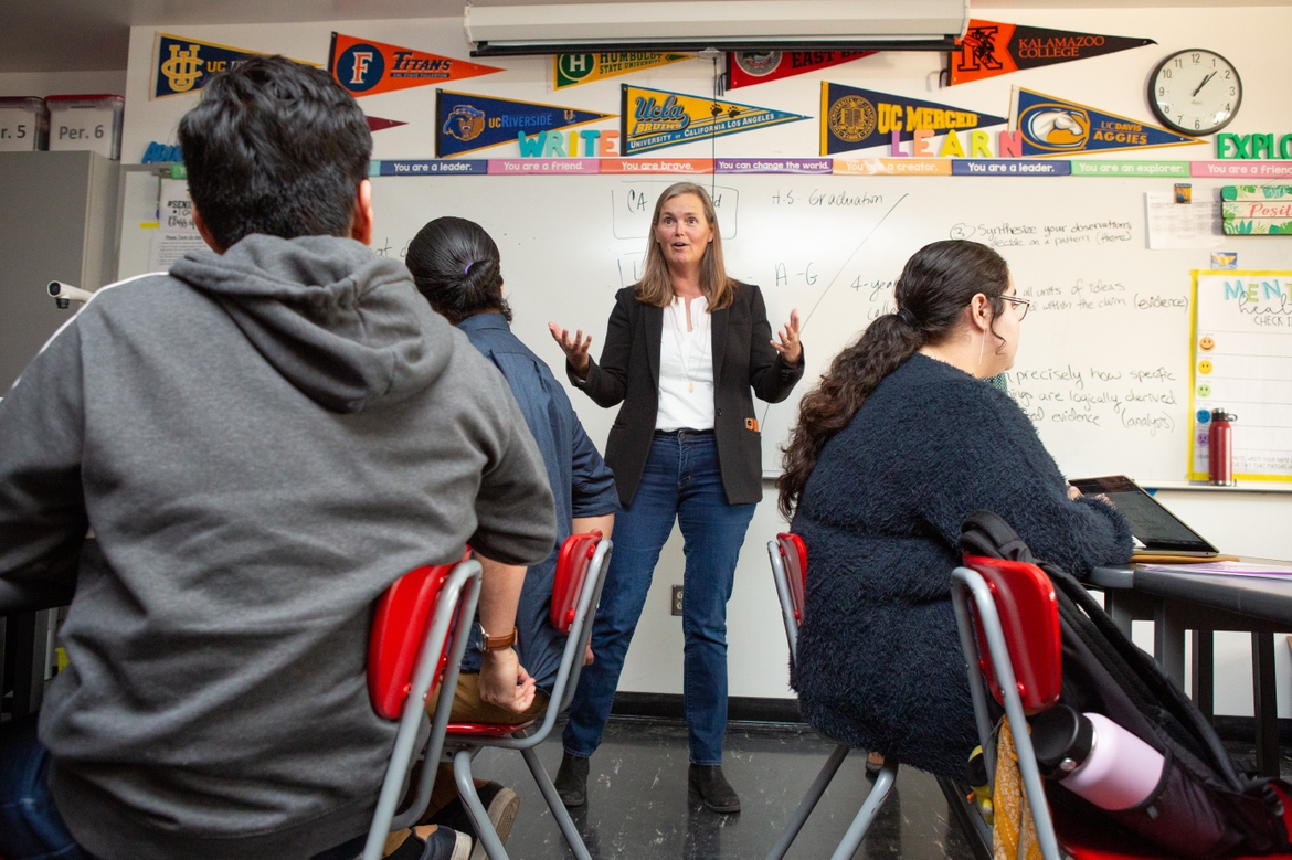 A school counselor speaking to students in a classroom in front of a whiteboard.