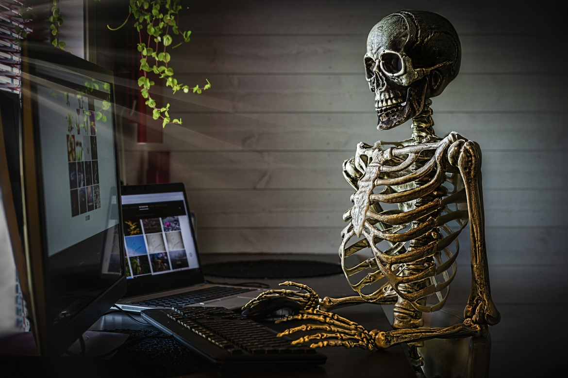 Skeleton typing on computer while sitting at a desk.