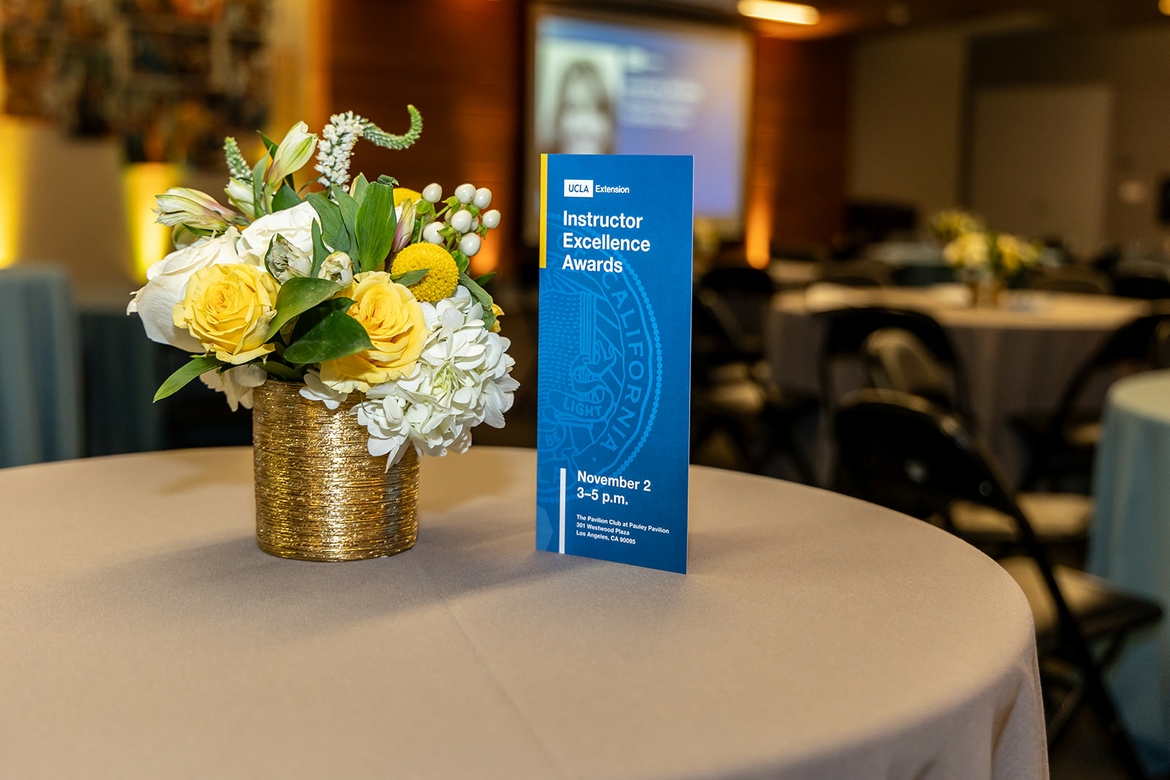 UCLA Extension Instructor Excellence Awards card atop a table beside flowers during the ceremony.