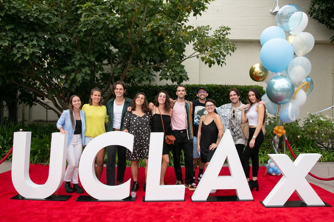 A group of UCLA x Film Fest Attendees together and pose for a photo in front of White UCLA X Sign