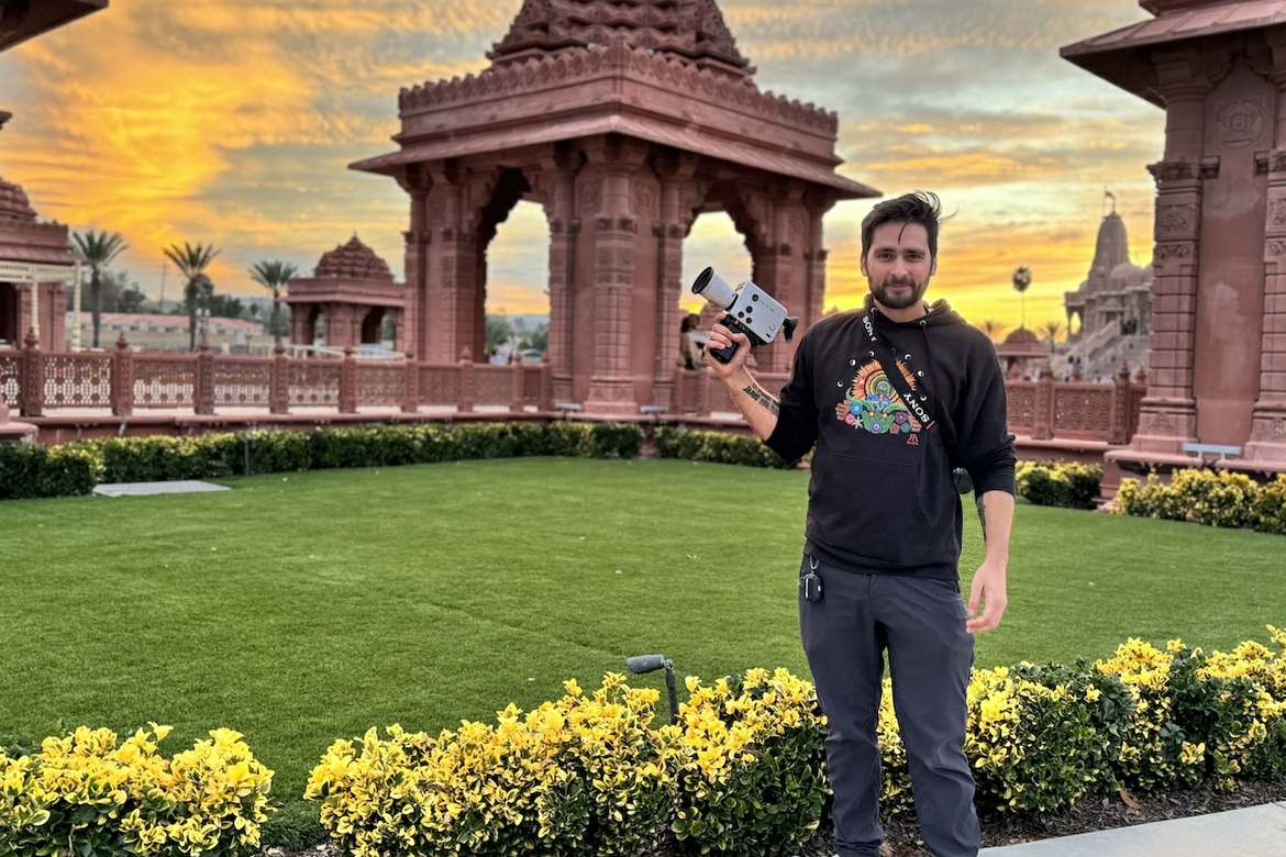UCLA Extension graduate Lukas Valderrama in front of flower beds holding his camera