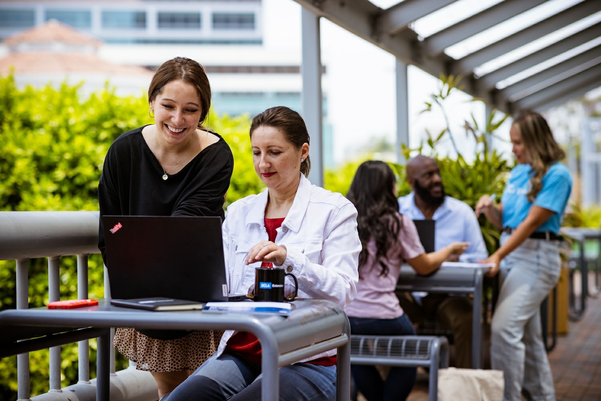 UCLA Extension workers are outside doing work on their laptops.