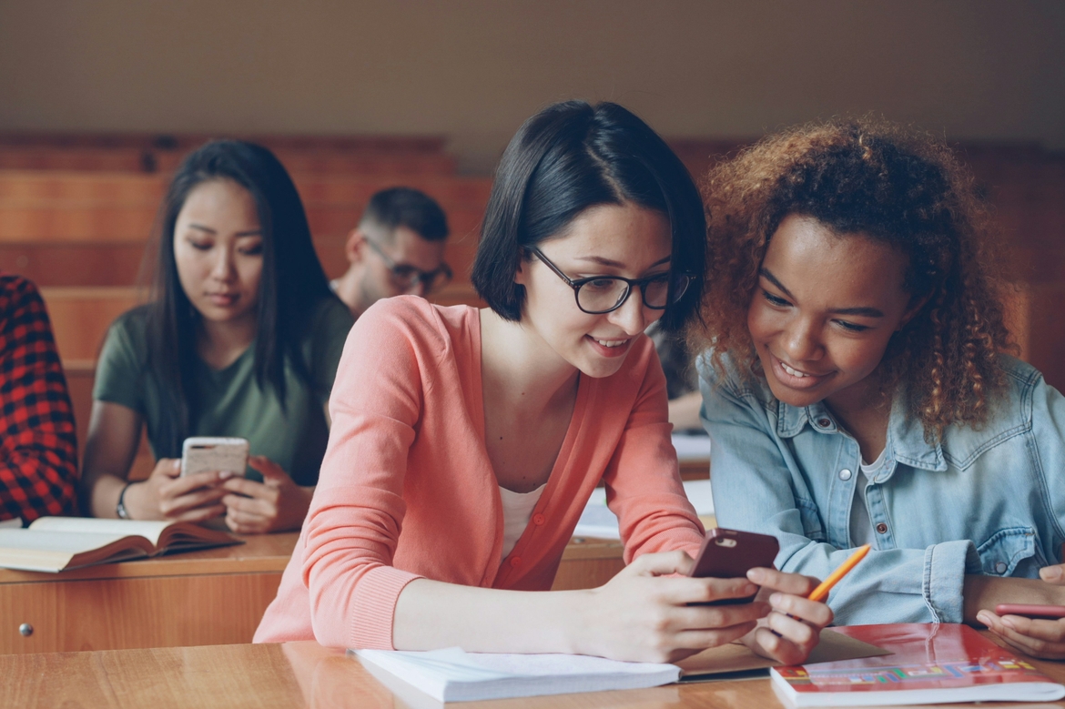 Students sit at a desk looking at a smartphone