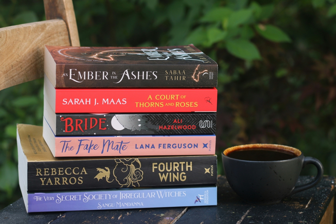A stack of romantasy books next to a coffee mug
