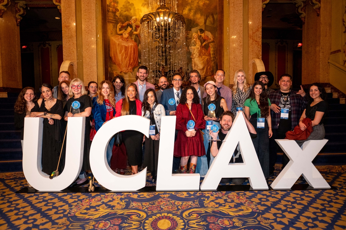 UCLAxFilmFest winners pose behind a large UCLAx Sign in front of a fountain at the Los Angeles Theatre