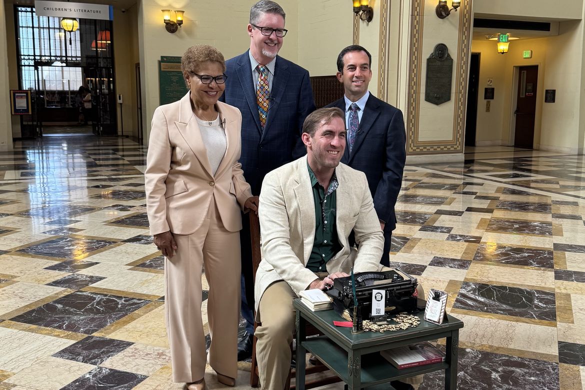 New poet laureate Brian Sonia-Wallace sits with a typewriter in the downtown library with city dignitaries