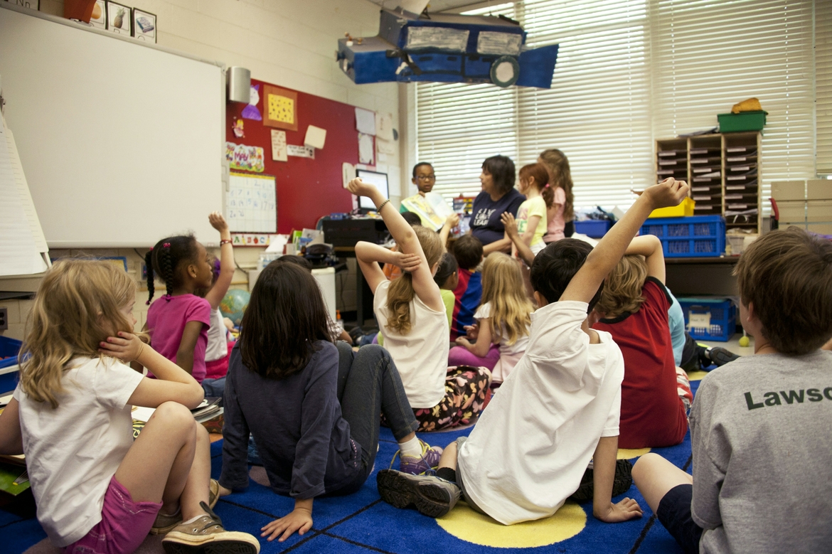 Young children raise their hands in an early childhood education classroom