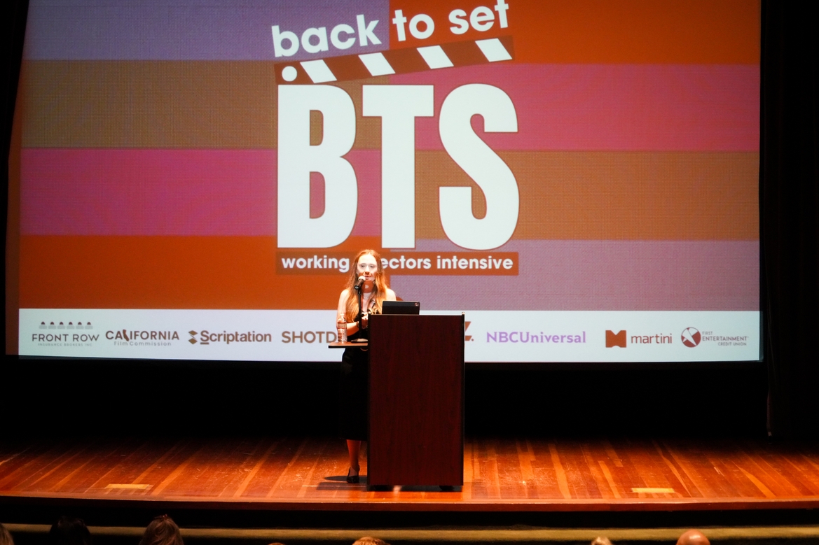 Kylie Eaton speaks at a podium in front of an auditorium for a program called Back to Set