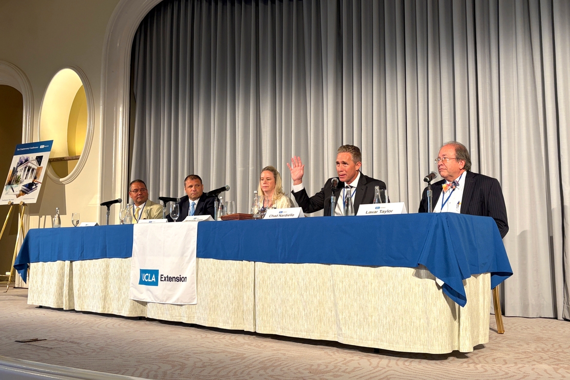 Four panelist speak at a table in the front of the ballroom