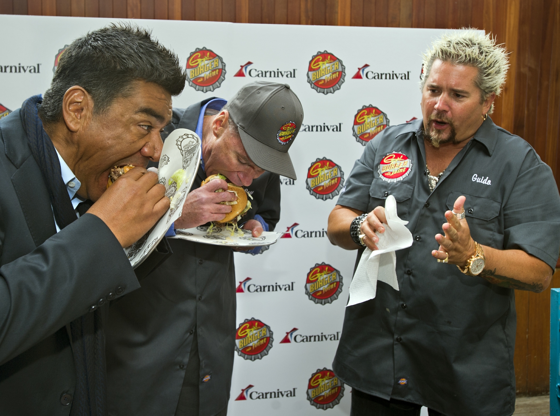 George Lopez and Gerry Cahill, President and CEO of Carnival Cruise Lines, sample new burger created by Guy Fieri in New York
