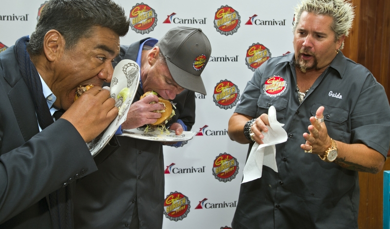 George Lopez and Gerry Cahill, President and CEO of Carnival Cruise Lines, sample new burger created by Guy Fieri in New York