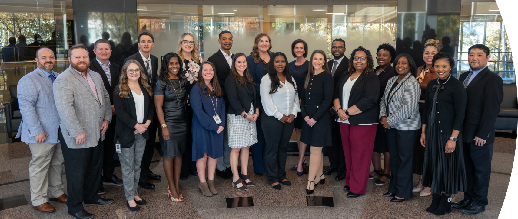 A diverse group of twenty-three professionally dressed people stand together in a modern office lobby.
