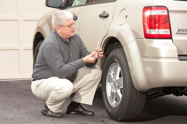Senior driver looking at tire pressure gauge
