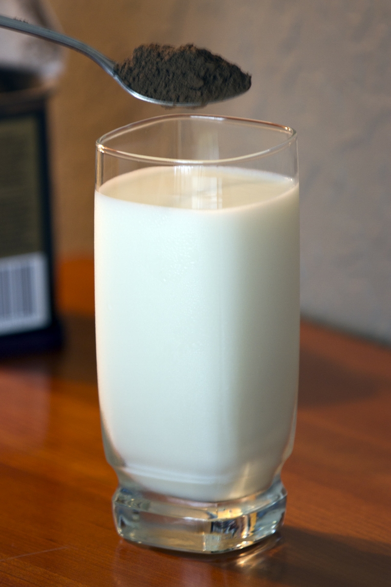 Cocoa Powder with spoon of cocoa above glass of milk