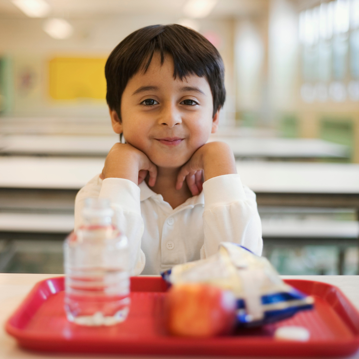 A young boy smiles with a cafeteria tray in front of him with healthy food and water