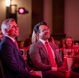  Two men smile and laugh at on-stage entertainment at Tarrant County Go Red event