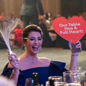 Woman smiles holding sign 'Our Table Has a Full Heart'